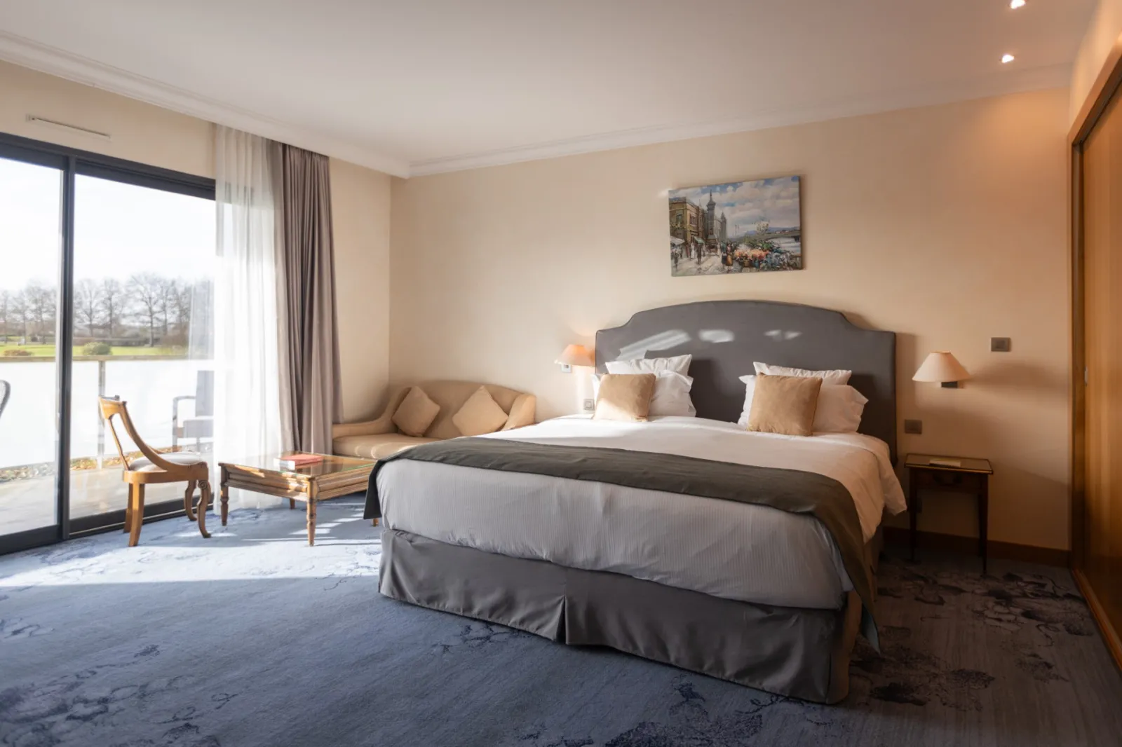 Elegant hotel bedroom with king-size bed, gray headboard, beige cushions, panoramic park view, light wood furniture, warm and modern décor at Hotel Le Relais de Margaux in Bordeaux