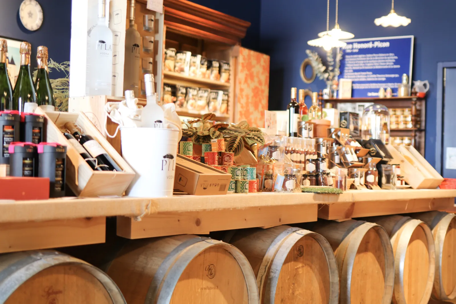 Regional Bordeaux shop display featuring wooden wine barrels, shelves of local products, champagne bottles, and gourmet items on a wooden counter, with blue and gold décor.