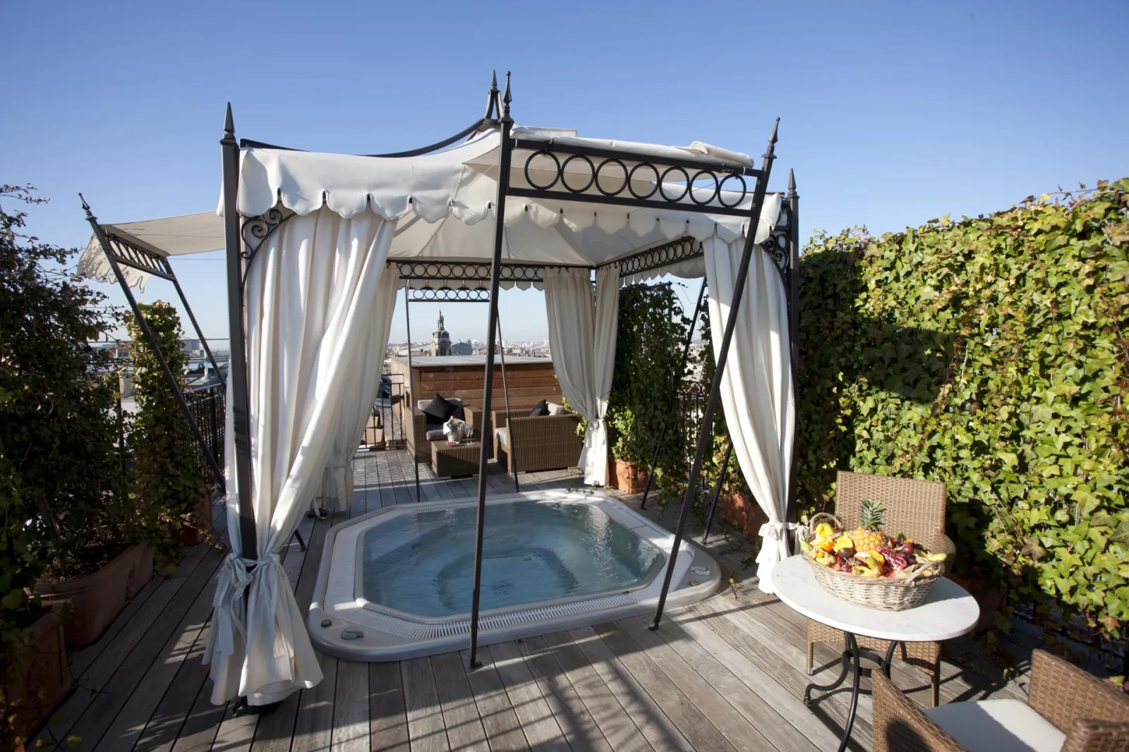 Luxury spa terrace featuring a hot tub under white canopy, surrounded by greenery with Bordeaux skyline view
