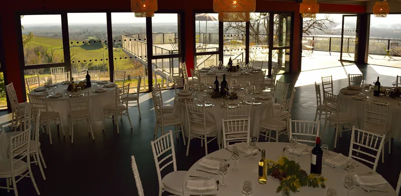 Reception hall at Château Réaut featuring set tables, white chairs, and large windows overlooking Bordeaux vineyards and countryside.