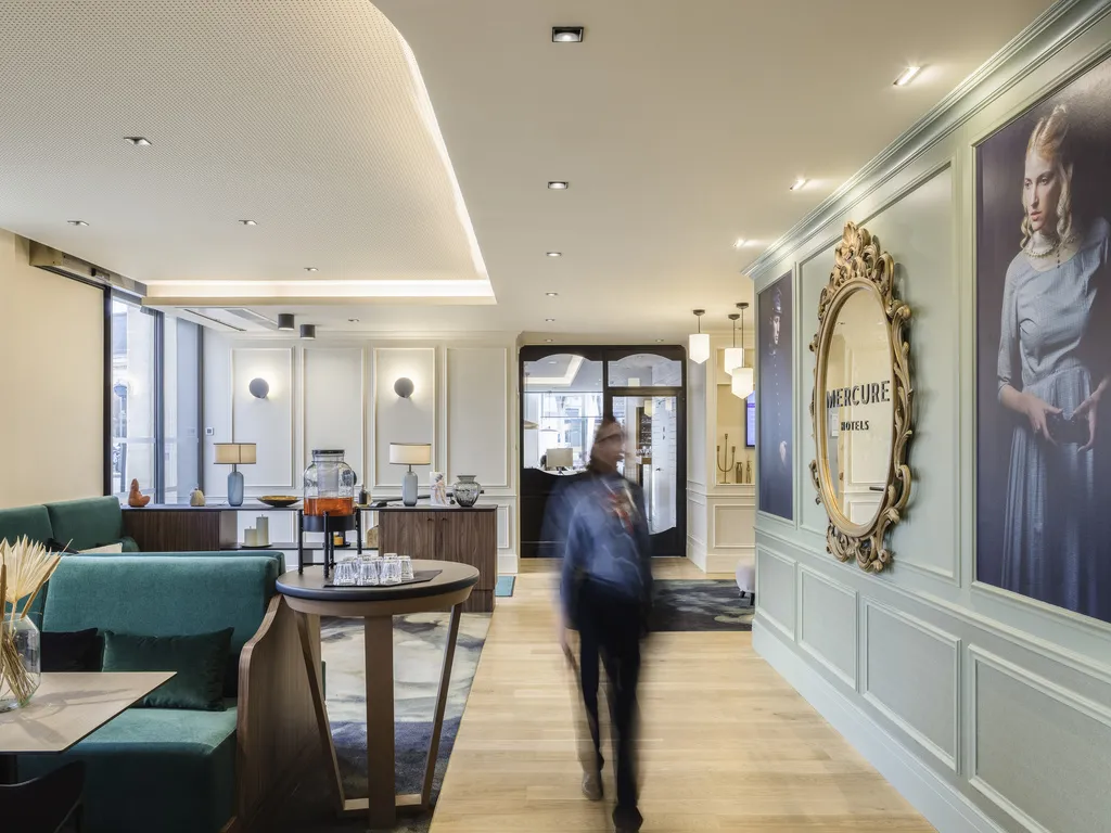Modern lobby of Mercure Bordeaux Gare Atlantic hotel featuring contemporary teal seating, ornate golden mirror, portrait artworks, and a guest walking through the space
