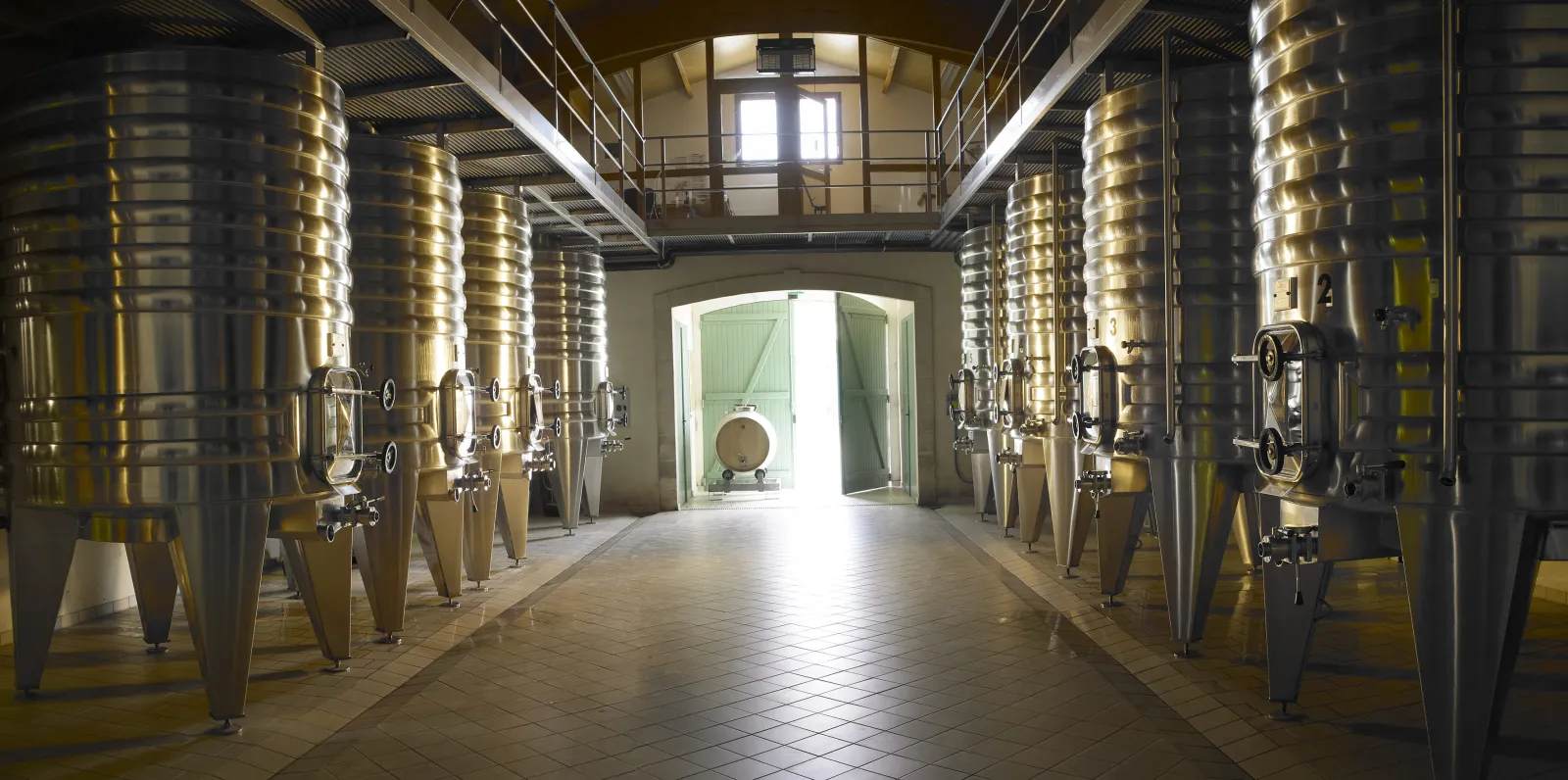 Interior of a winery with rows of stainless steel fermentation tanks lining a central aisle at Château La Rose Perrière in Bordeaux.