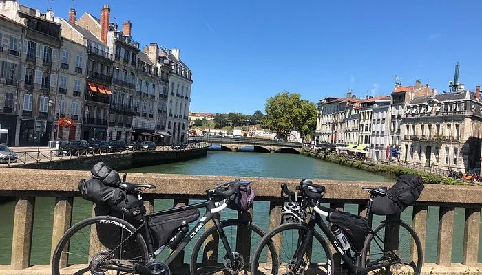 Two black-pannier equipped bicycles parked on a bridge overlooking the Garonne river in Bordeaux, with views of the riverside buildings and classical architecture.