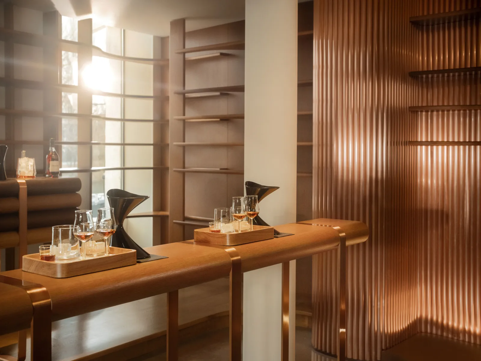 Elegant tasting room at Hennessy in Bordeaux featuring a curved wooden counter, cognac glasses, modern furnishings, large windows, and wooden slatted shelving.