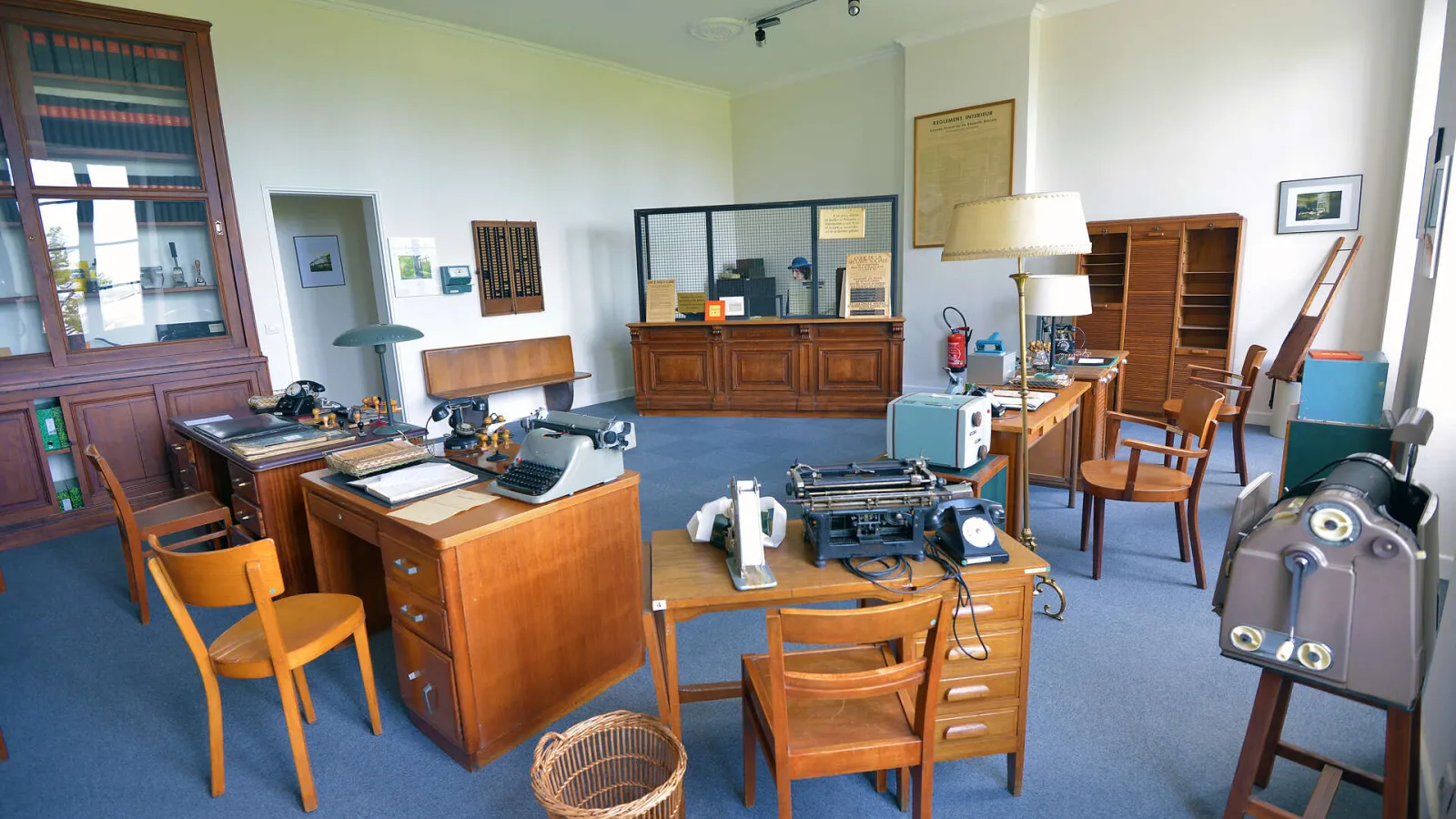 Interior of the National Museum of Health Insurance in Bordeaux displaying a historical office with wooden furniture, typewriters, vintage communication equipment, and period documents on a blue floor.