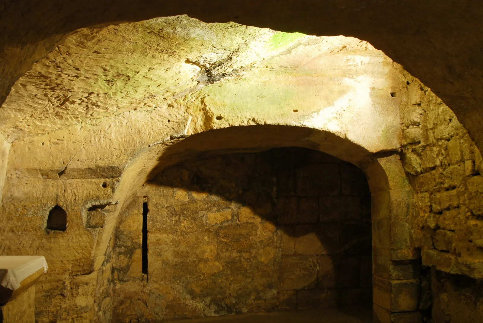 Vaulted stone gallery with a lit archway entrance in the limestone catacombs of Saint-Émilion