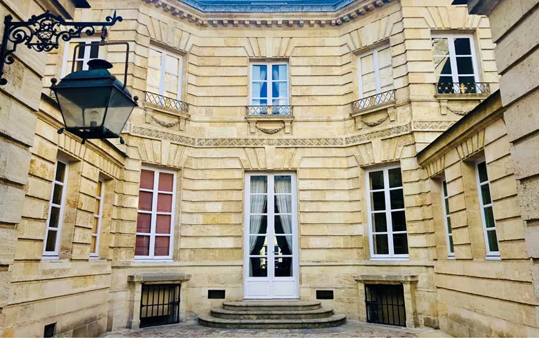 Interior courtyard of the small Labottière mansion in Bordeaux, featuring symmetrical ashlar stone facade, evenly spaced windows, central entrance door, and ornamental wall lantern.