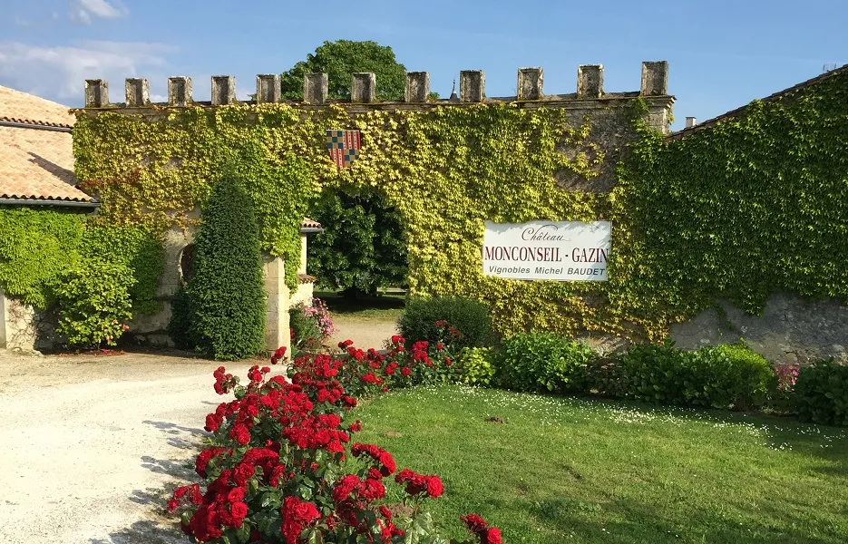 Château Monconseil-Gazin in Bordeaux with ivy-covered stone walls, red rose bushes in the foreground, and a vineyard sign
