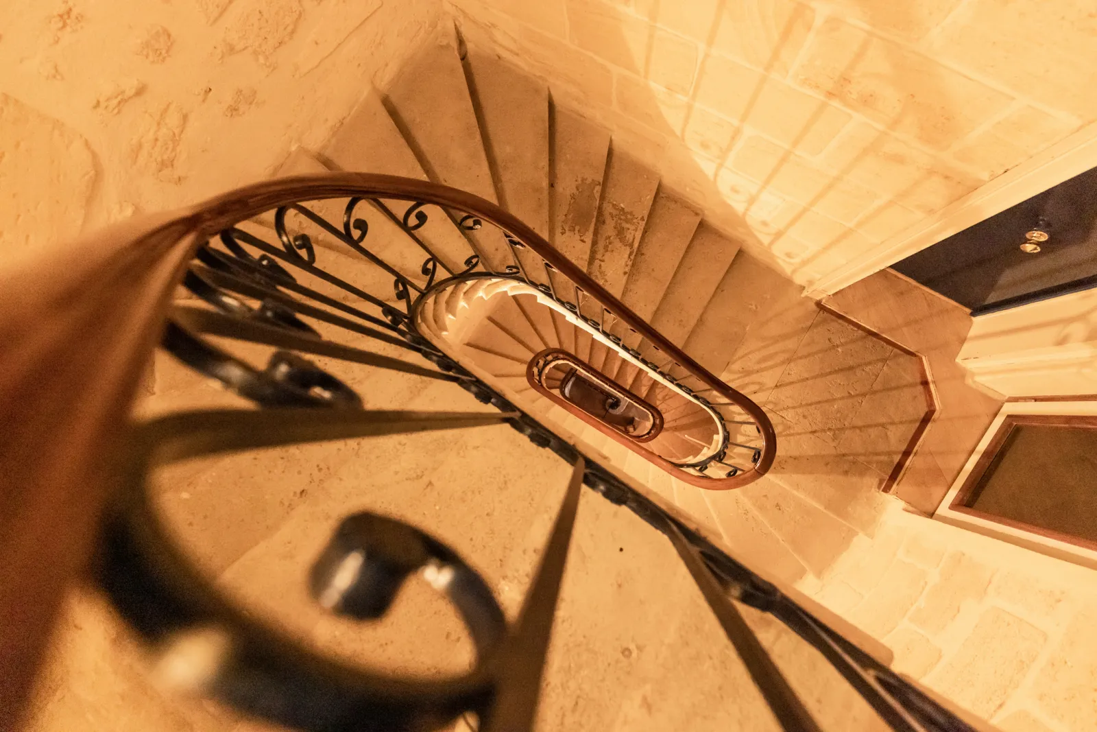 Overhead view of a spiral staircase with wrought iron railing at the Hôtel de la Tour Intendance in Bordeaux, featuring radiating steps and cast shadows.