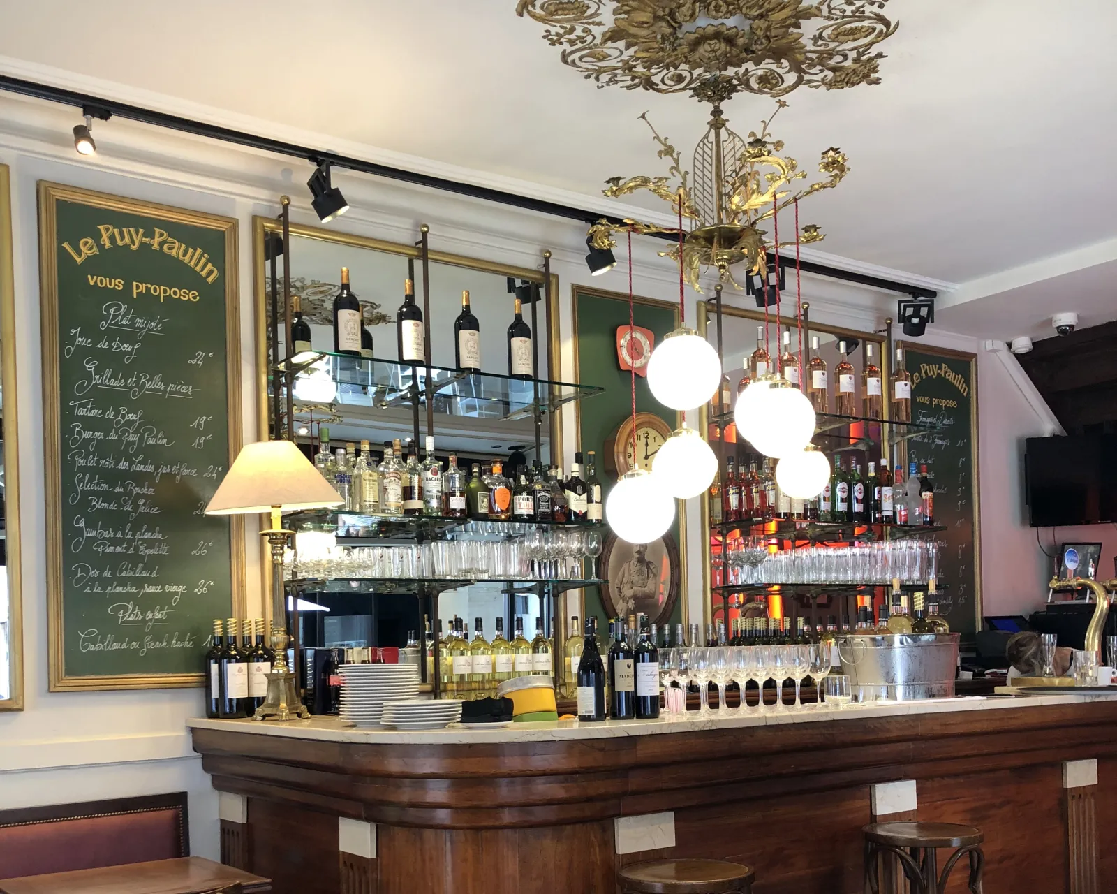 Elegant Le Puy-Paulin bar in Bordeaux featuring dark wood counter, wine bottle shelves, chalkboard menus, modern pendant lights and vintage décor.