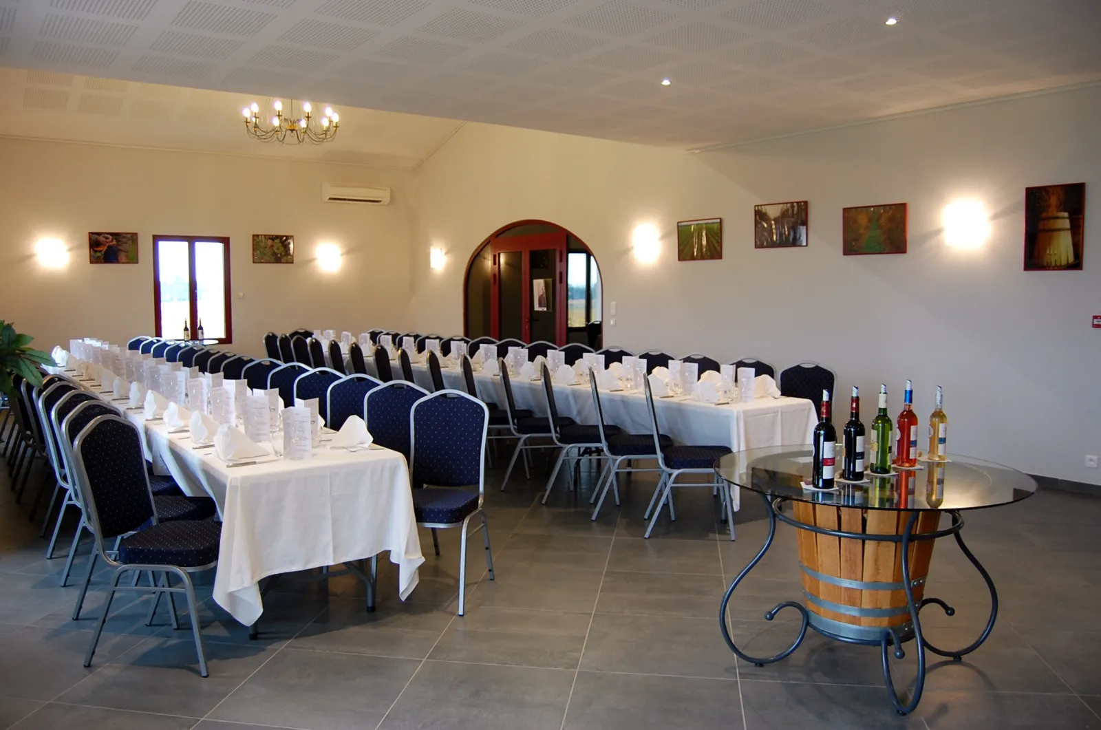 Elegant reception hall at Château Pichon Bellevue in Bordeaux featuring white-dressed tables, blue and black chairs, wine bar with bottles, and sophisticated wall décor