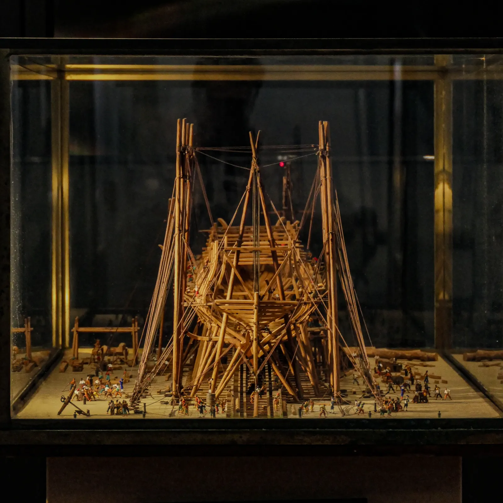 Wooden ship model with rigging and sails surrounded by miniature figures displayed in a glass case at the Bordeaux Maritime History Museum