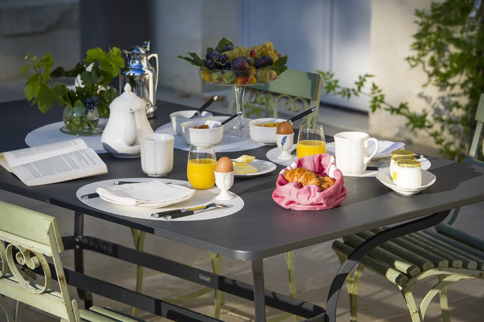 Elegant breakfast table set on a terrace with white tea service, orange juice, croissants, fresh fruits, flowers and cutlery at Chartreuse Haut-Bailly in Bordeaux