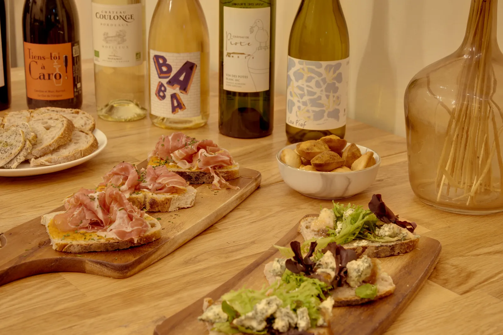 Bordeaux wine tasting table featuring white wine glasses, open-faced sandwiches with cured ham and blue cheese, toasted bread, roasted potatoes, and appetizers.