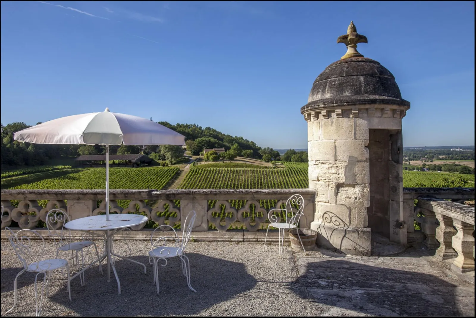 Terrace at Château de La Rivière overlooking Bordeaux vineyards, white garden furniture, parasol and stone fortified tower