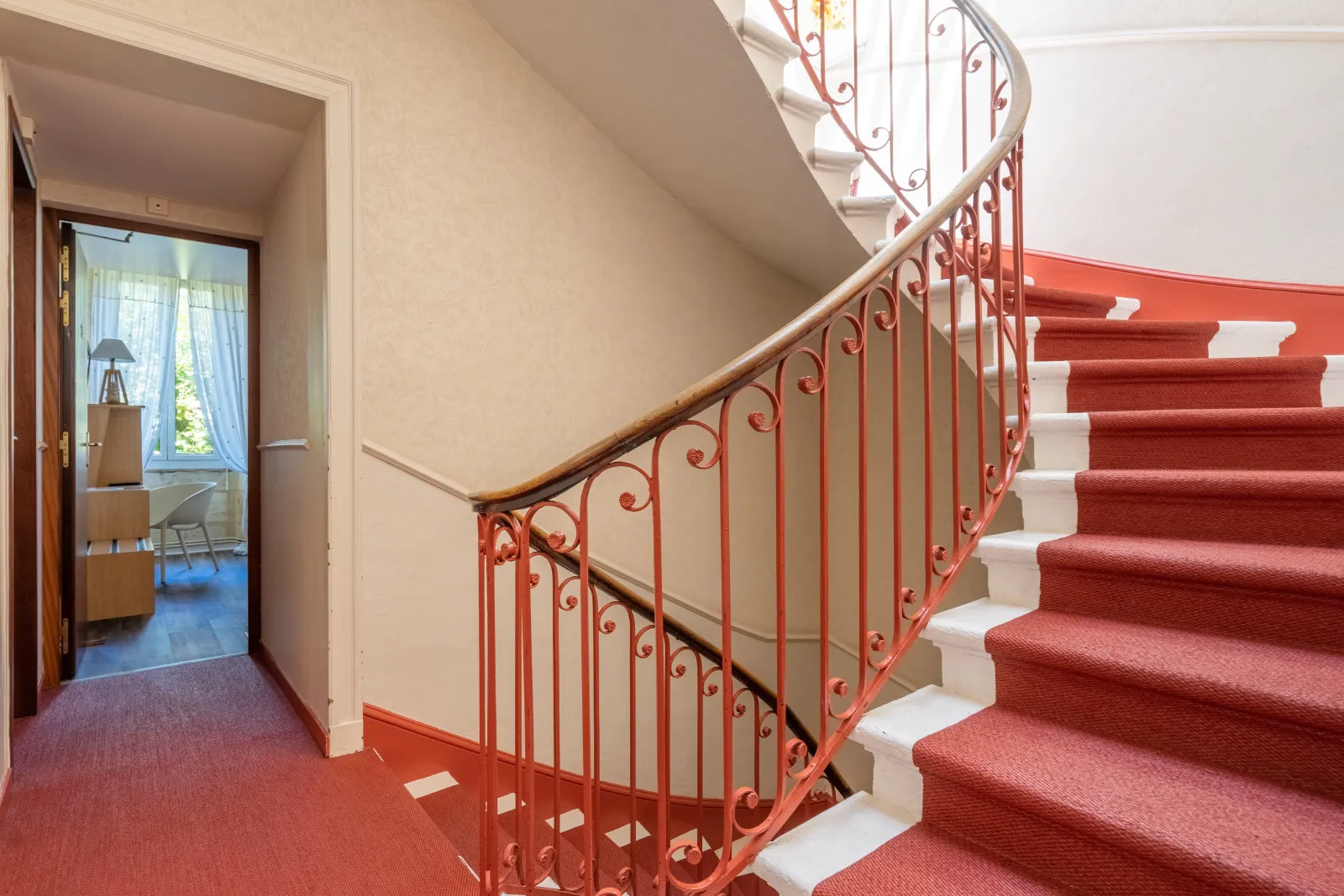 Spiral staircase with red wrought iron railing, white steps and red carpet runner in the hallway of Hotel des Voyageurs in Bordeaux