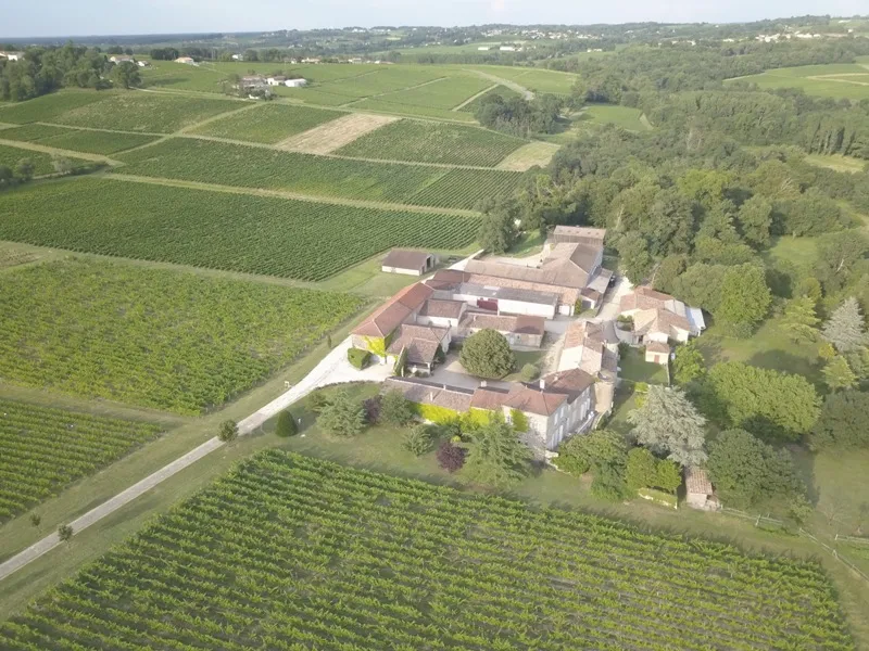 Aerial view of Château Monconseil-Gazin surrounded by vineyards in the Bordeaux region, featuring red-tiled roofs and landscaped gardens.