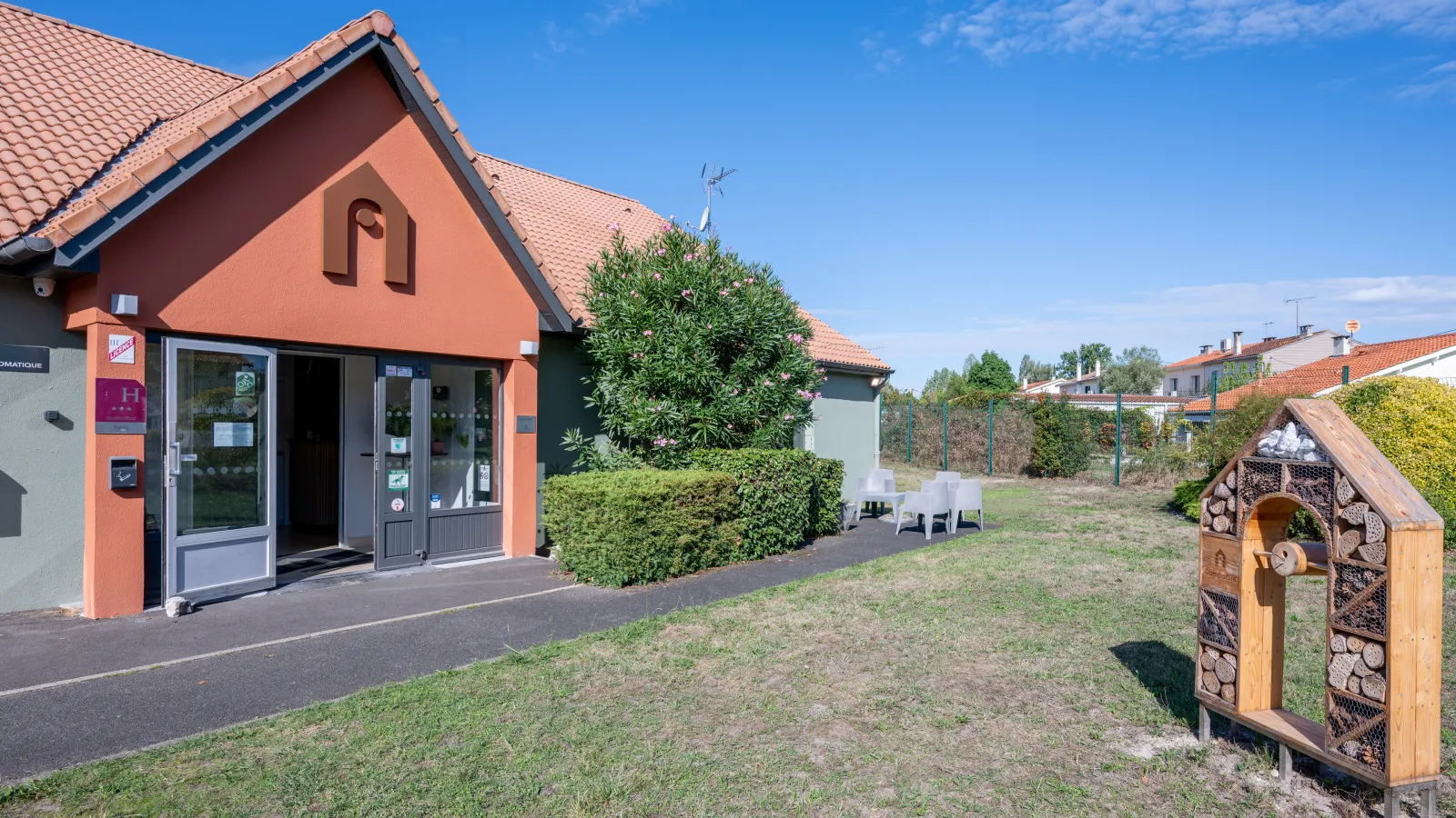 Orange and black reception building of a Campanile hotel with tiled roof, surrounded by a garden with deck chairs and a decorative wooden shelter, in Gradignan near Bordeaux.