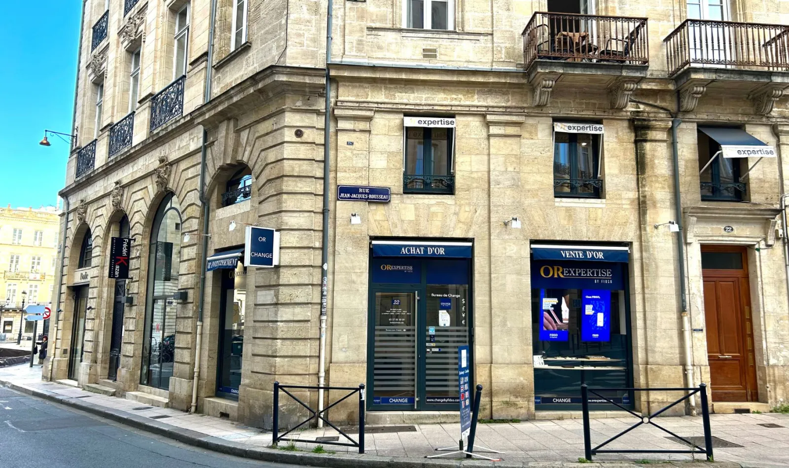 Haussmannian building facade in Bordeaux with ground floor shops, including a jewelry store OR EXPERTISE and a currency exchange office, on Jean-Jaurès street.