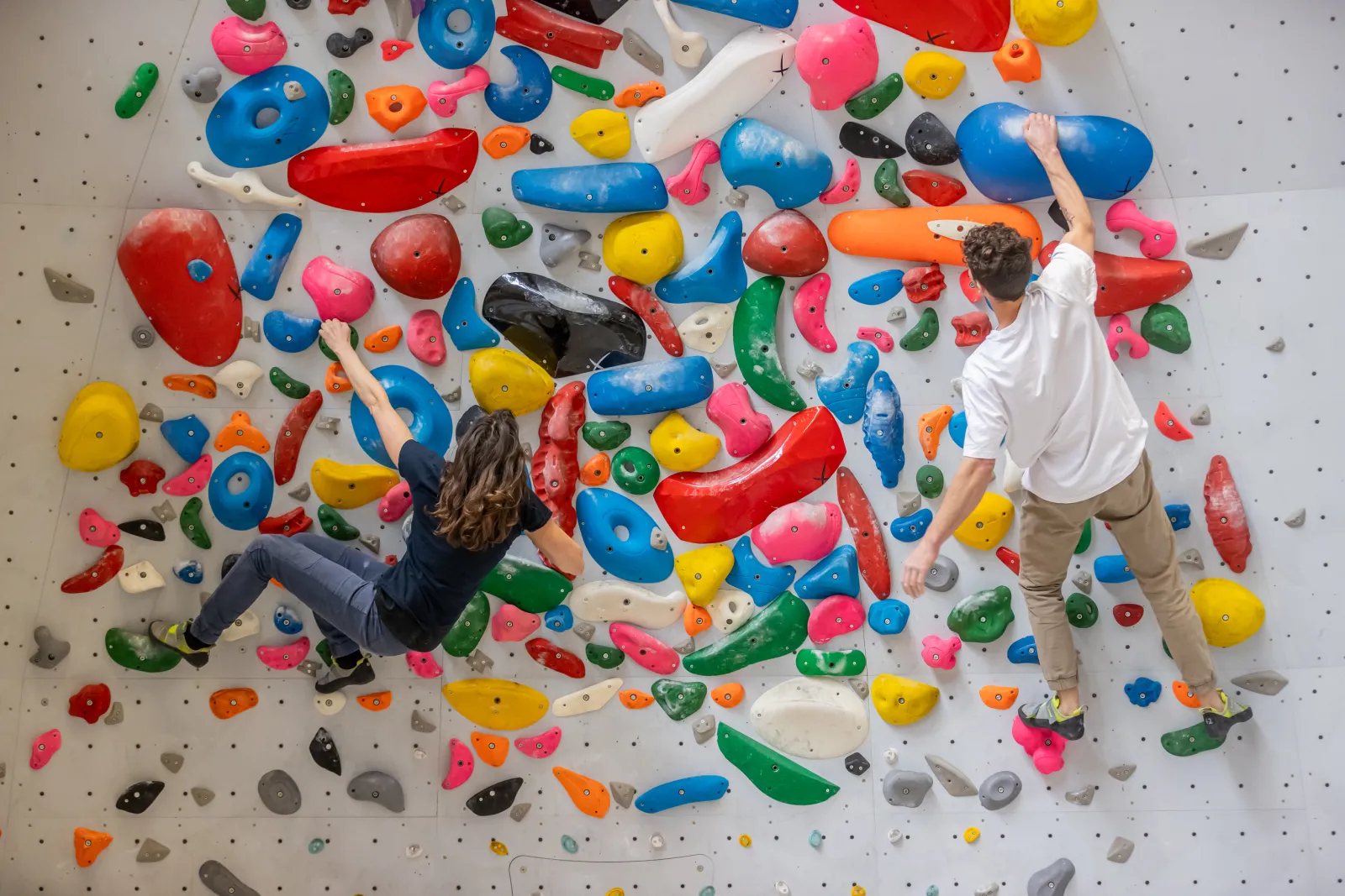 Two climbers scaling a colorful indoor climbing wall with various holds in blue, red, yellow, green, pink, and orange at UCPA Sport Station in Bordeaux.