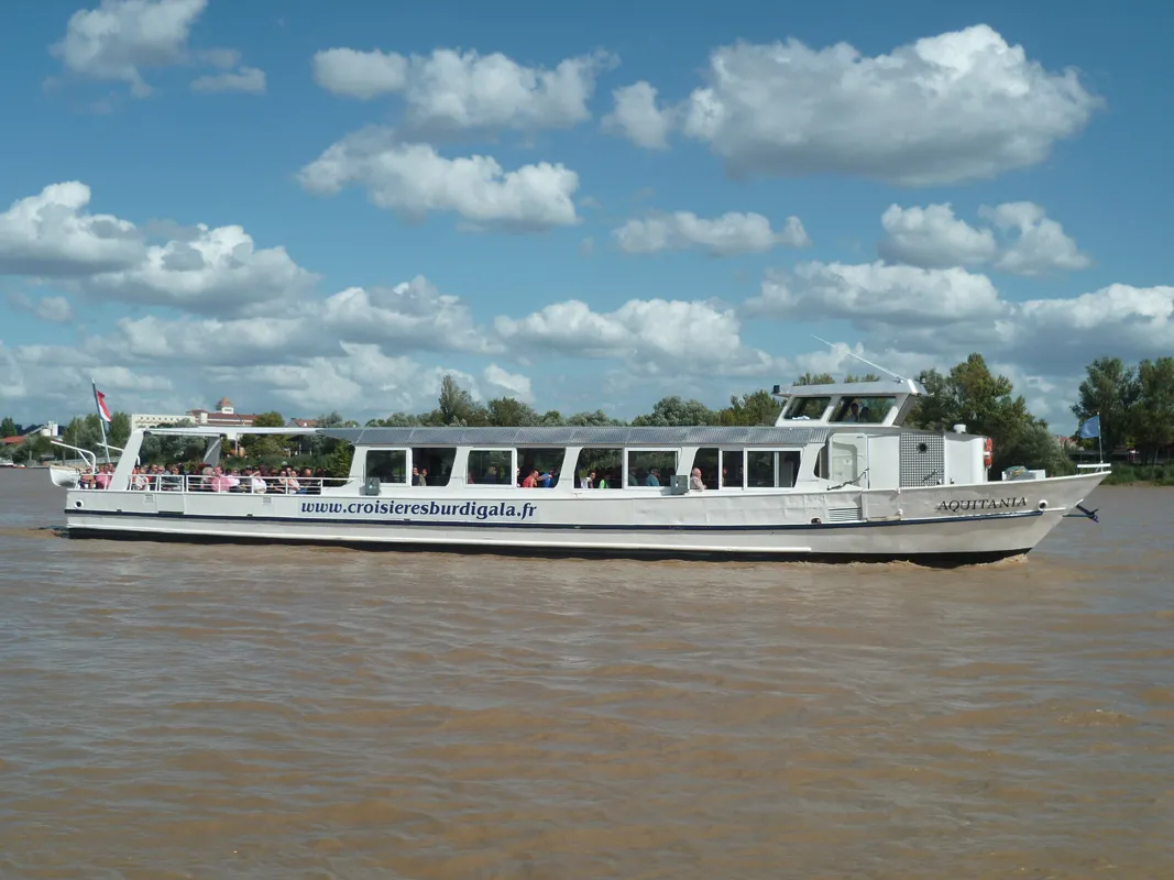 The cruise boat Aquitania sails on the Garonne river in Bordeaux, a white river tourism vessel with passengers visible on board.
