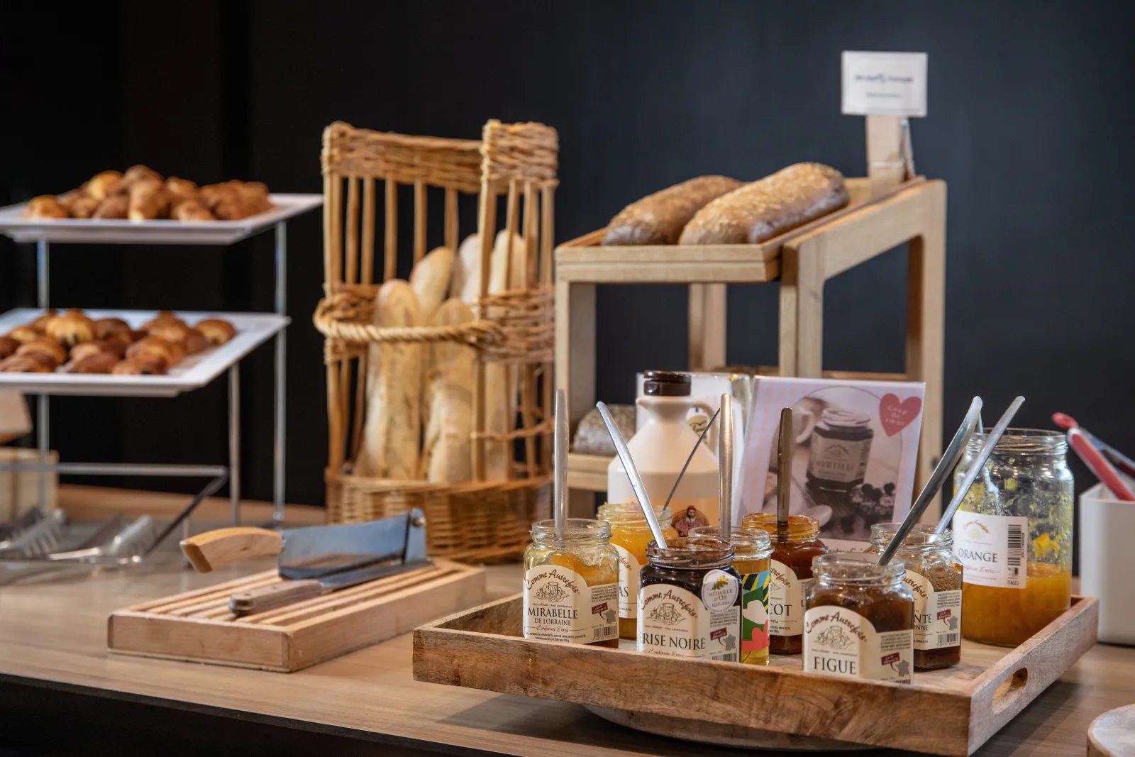 Breakfast buffet display at Novotel Bordeaux Mérignac featuring pastries, fresh bread, artisanal jams, juices, and wicker baskets on wooden serving tables