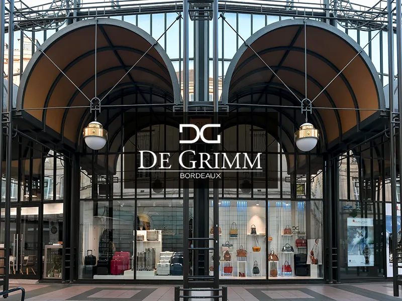 De Grimm luxury leather goods store in Bordeaux, featuring an elegant arched canopy, window displays showcasing designer handbags and fashion accessories.