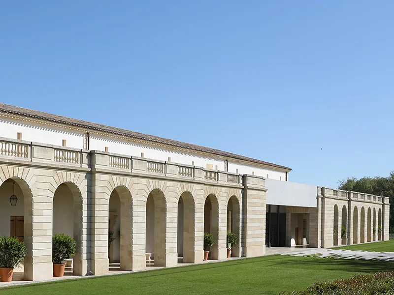 Neoclassical façade of Château Marquis d'Alesme Becker in Bordeaux, featuring a colonnade, balustrade terrace, and manicured lawn.