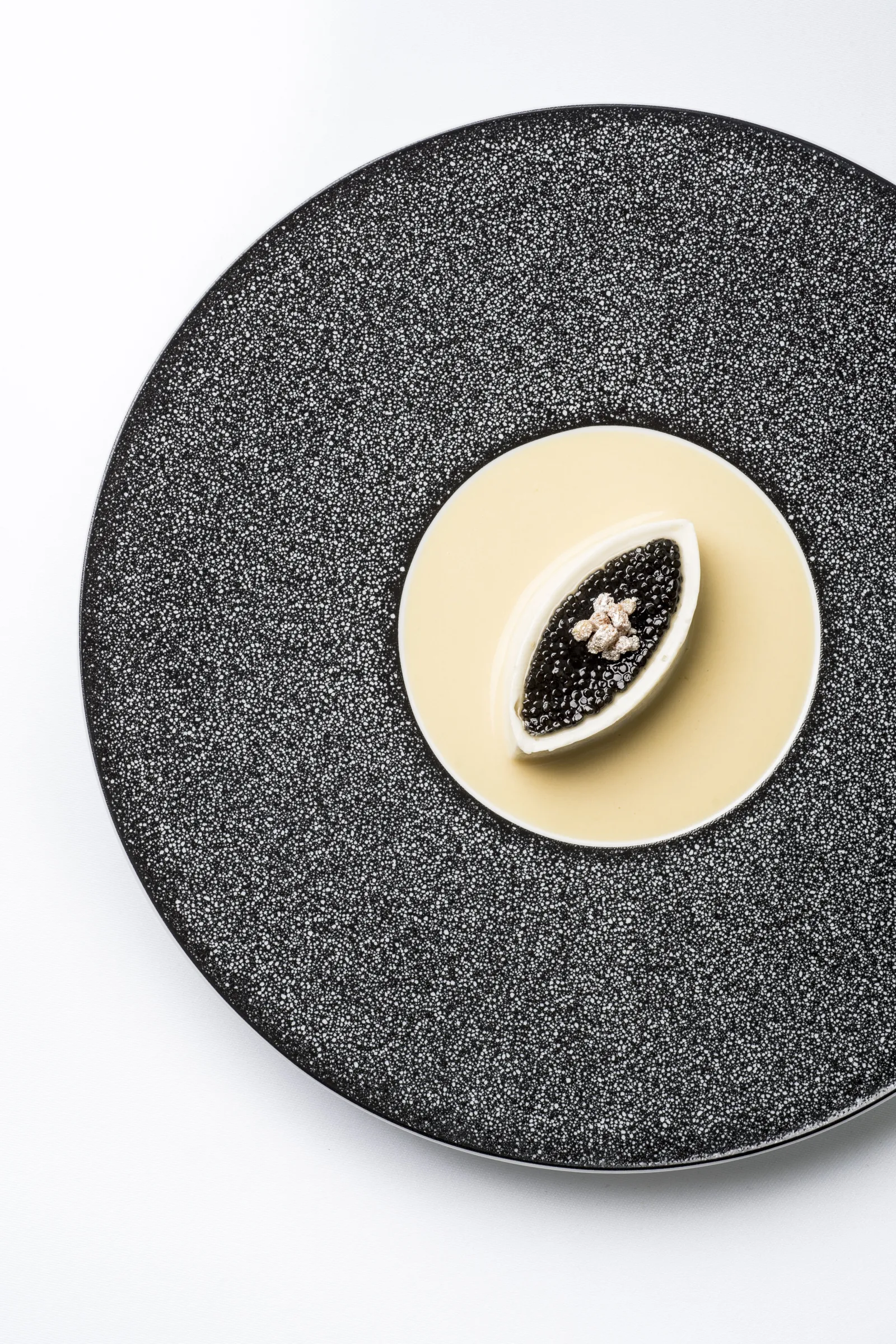Gourmet plate from Lalique restaurant in Bordeaux: black caviar served in a white shell on a textured black plate, accompanied by cream pearls.