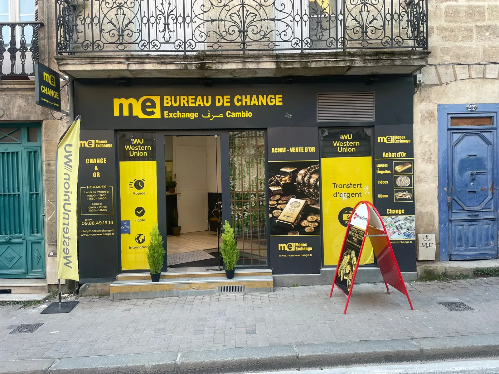 Monex Exchange currency exchange storefront in Bordeaux on Victor Hugo street. Modern black and yellow facade displaying Western Union and gold buying services, flanked by traditional blue and green Bordeaux doors.