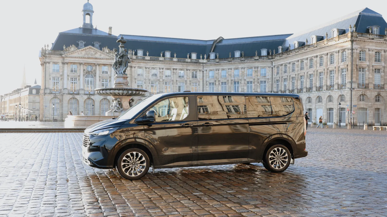 A black minivan parked on Place de la Bourse in Bordeaux, facing the historic 18th-century buildings and central equestrian statue