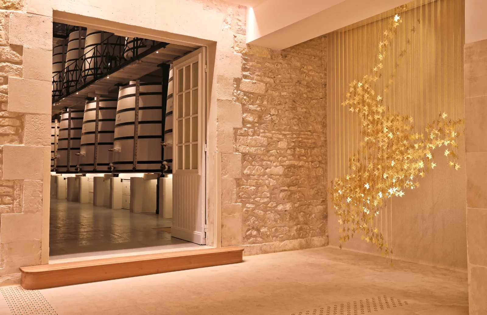 Interior of Maison Rémy Martin in Bordeaux featuring exposed stone walls, cognac barrels visible in the back room, and golden leaf-shaped wall decoration