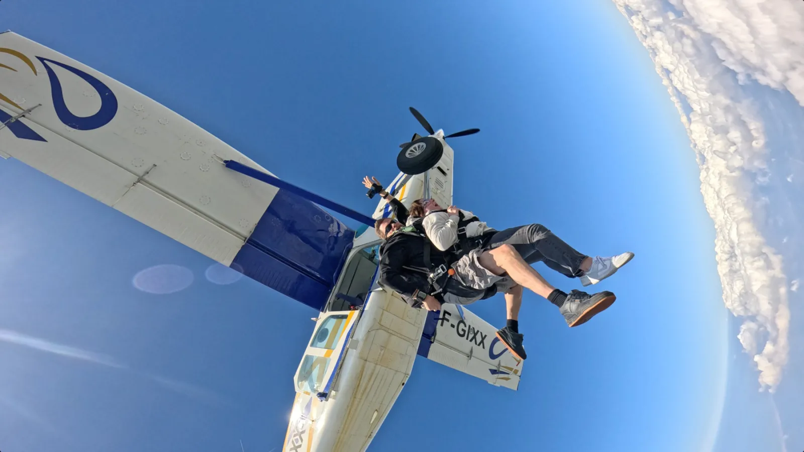 A skydiver in freefall jumps from a propeller aircraft over Bordeaux against a clear blue sky.