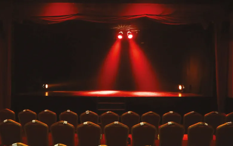 Stage of the Chartrons Theater in Bordeaux lit by red spotlights, with rows of golden seats in the foreground