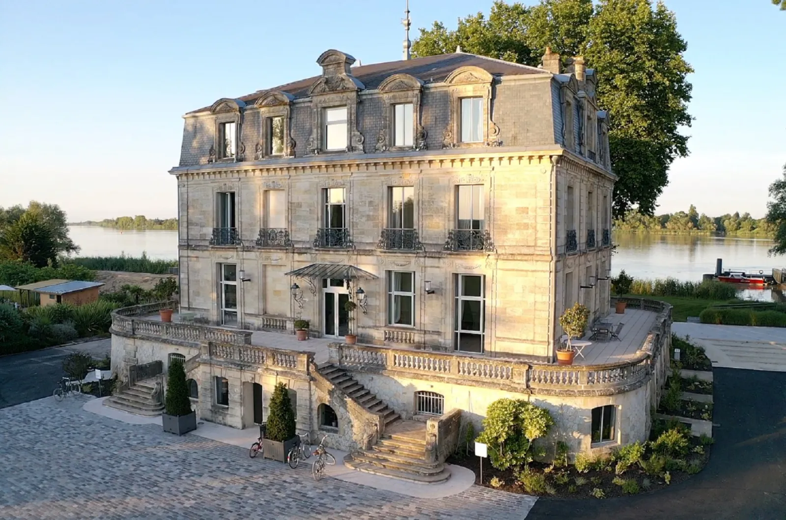 Château Grattequina in Bordeaux, a 19th-century stone mansion with mansard roofs overlooking the Garonne river, featuring ornamental terraces and wrought-iron balconies.