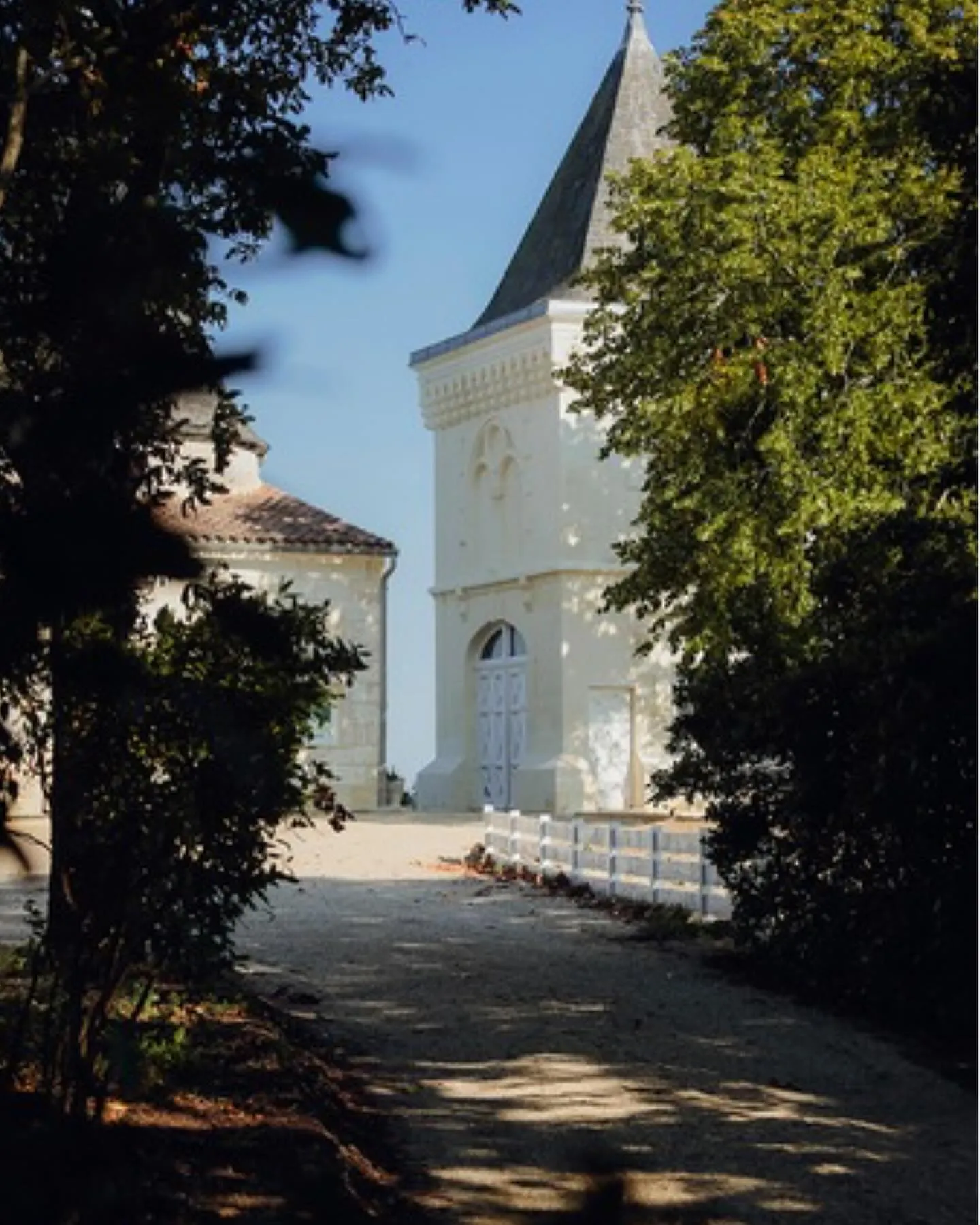 White chapel with a pointed black steeple surrounded by greenery at Château CarlMagnus in Bordeaux