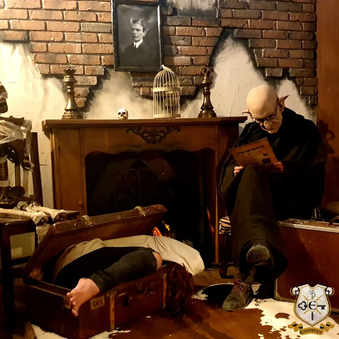 Crime scene reconstruction in a Bordeaux museum: a body lying on the floor in front of a fireplace, a bald character holding a newspaper, with period accessories and a framed photograph on the wall.