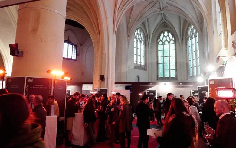 Crowd of visitors inside Espace Saint Rémi in Bordeaux, a Gothic church converted into an exhibition space with ribbed vaults, stained glass windows and pink columns.