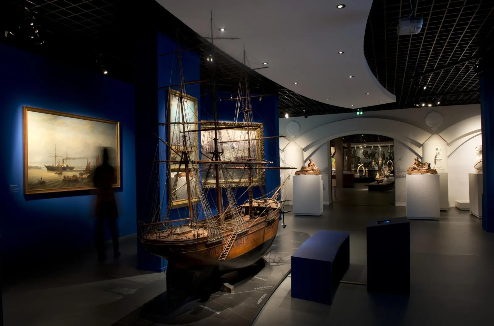 Maritime exhibition at the Museum of Aquitaine in Bordeaux displaying an 18th-century sailing ship model, maritime paintings, and sculptures on a blue background, showcasing Bordeaux's naval heritage.