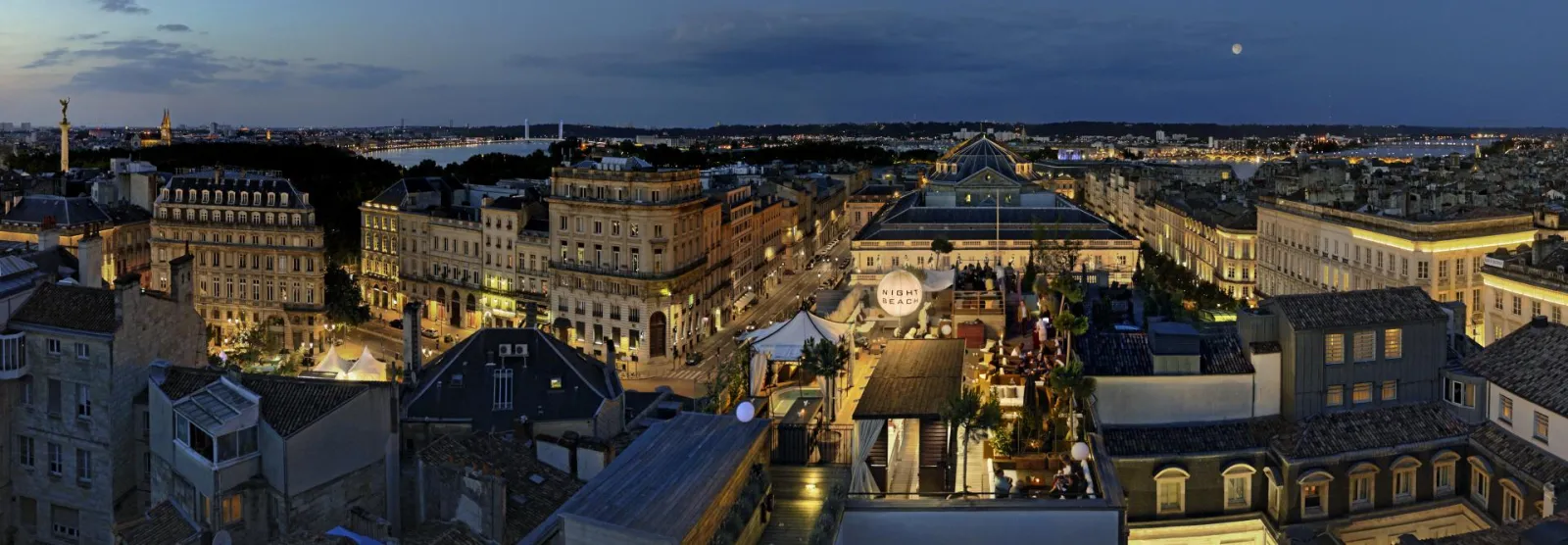 Night panoramic view of Bordeaux from the Intercontinental Grand Hotel terrace, featuring illuminated city center facades, the Garonne River, and urban skyline.