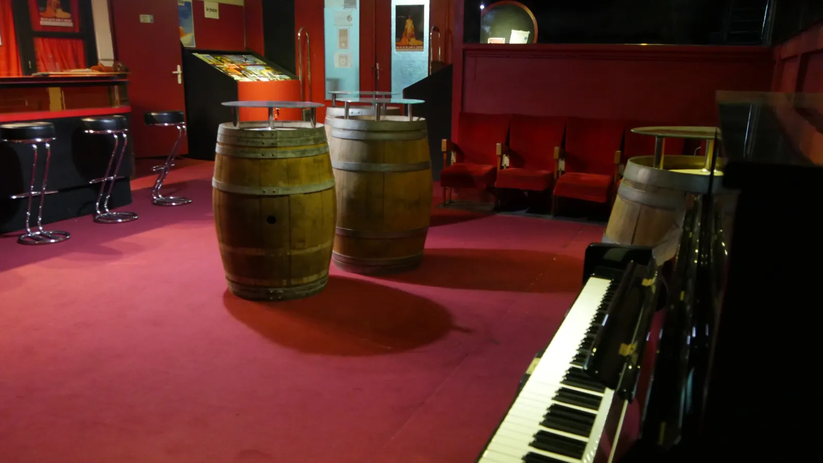 Interior of the Pont Tournant Theater in Bordeaux featuring red walls, wooden barrels, black grand piano, bar stools and informational displays