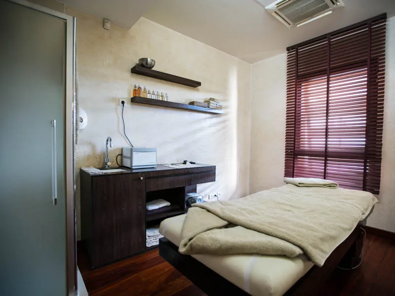 Minimalist spa bedroom featuring a double bed, dark wood desk, wall shelves, burgundy blinds and attached bathroom at Les Bains de Margaux in Bordeaux