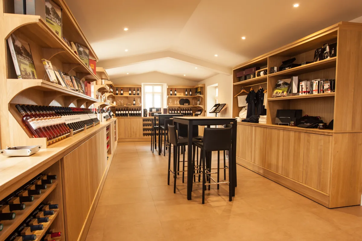 Elegant wine cellar interior featuring light wood walls, wine bottle displays, black tasting counter with stools, bookshelves with decorative items, and modern ceiling with integrated lighting.