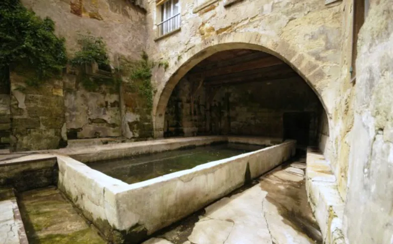 Stone basin in a paved courtyard surrounded by old stone walls with an arch, in the Old Lormont district of Bordeaux.