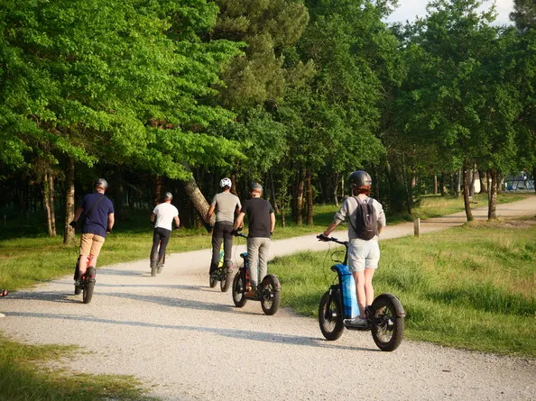 Group of people riding roller skates and electric scooters on a shaded path in a Bordeaux park, surrounded by green trees.