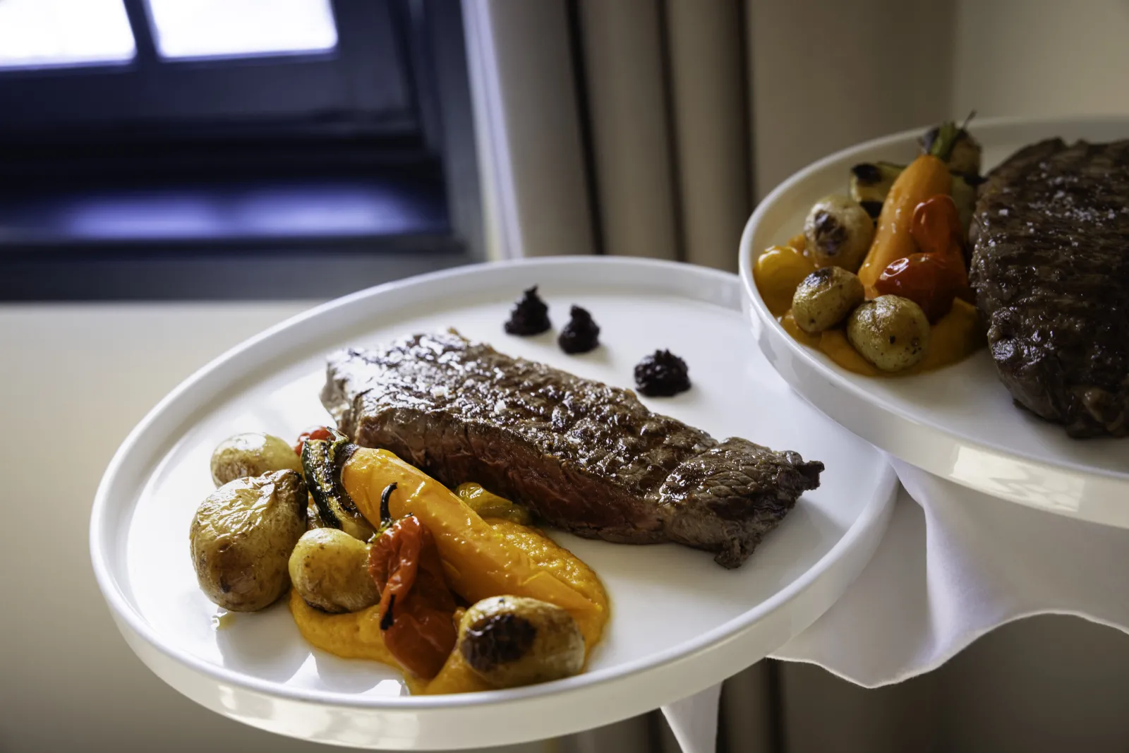 Two gourmet plates featuring grilled beef steaks with roasted vegetables including yellow peppers and mushrooms, along with golden roasted potatoes, served at L'Atelier de Candale in Bordeaux.