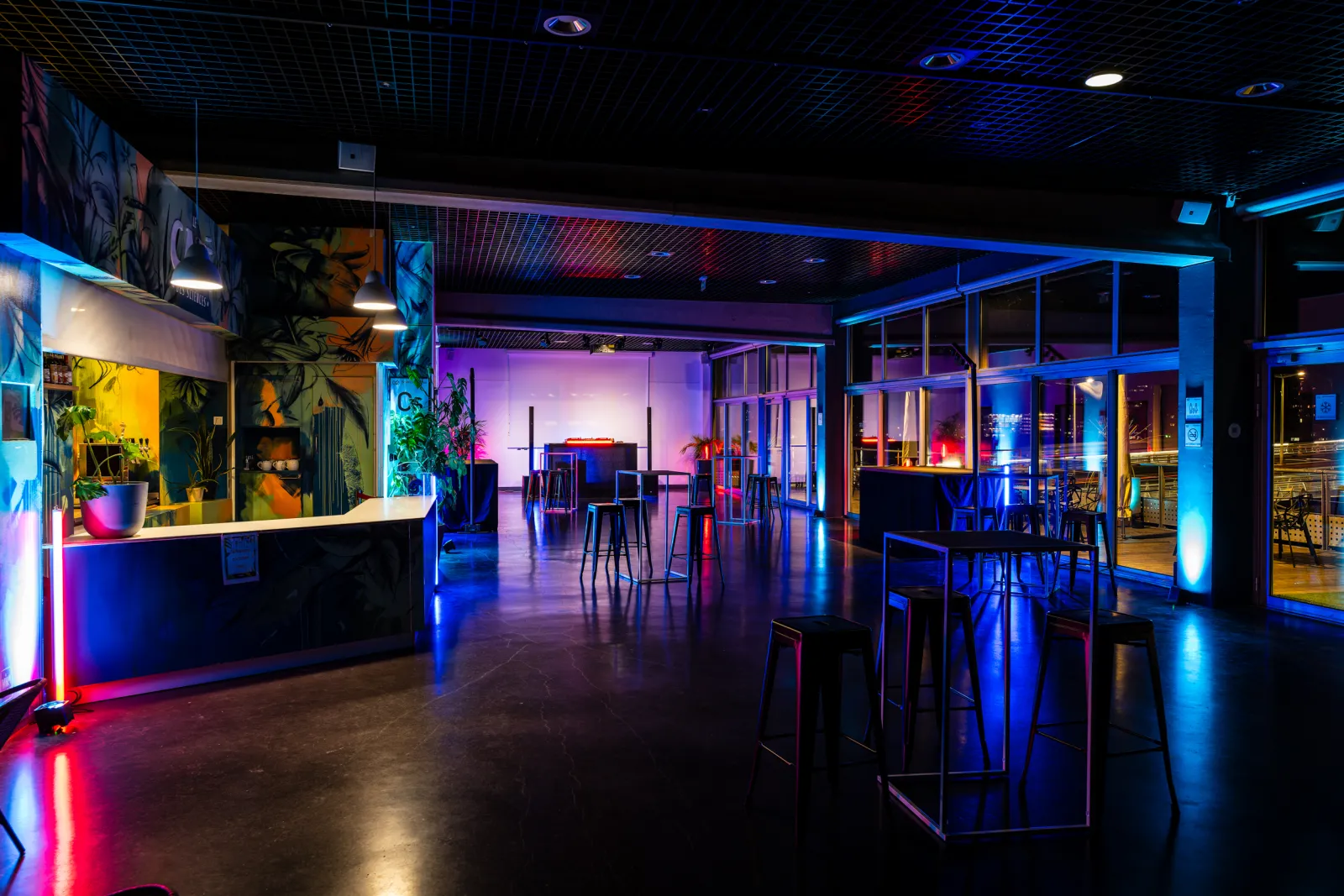 Futuristic interior of a scientific exhibition space featuring blue and pink LED lighting, reception counter, high stools, glass walls, and interactive installations at Cap Sciences in Bordeaux.