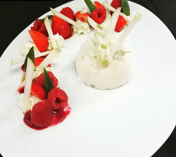 Gourmet plated dessert featuring a white mousse dome topped with apple shavings, surrounded by strawberries, raspberries and mint leaves arranged in a spiral pattern