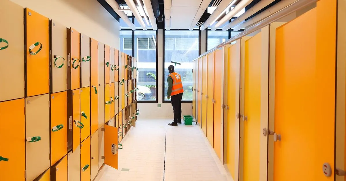 Corridor of orange and yellow lockers in a public swimming pool with a maintenance worker wearing an orange safety vest