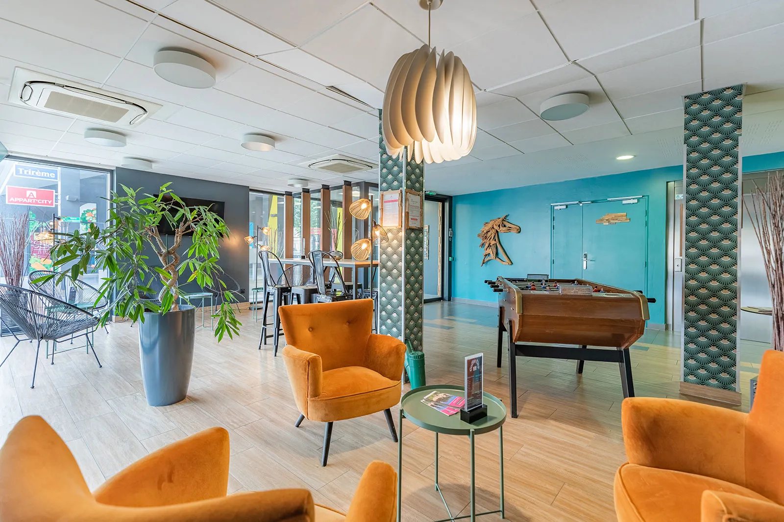 Modern lobby of Appart City Confort Bordeaux Chartrons featuring orange armchairs, designer pendant light, turquoise walls, foosball table and relaxation areas